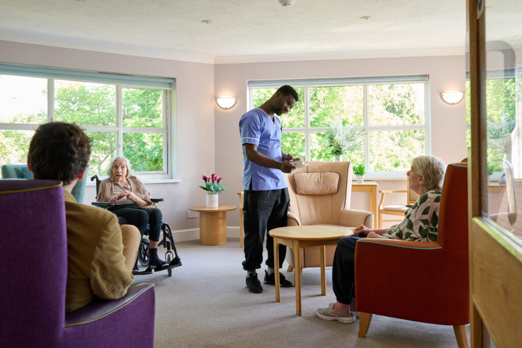 Male nurse offering a resident a cup of tea in the communal lounge.